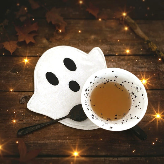 eisterförmiger Mug Rug mit einer Tasse Tee auf einem Holztisch, herbstliche Deko und funkelnde Lichter im Hintergrund.
